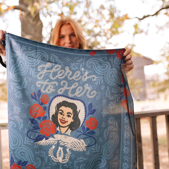 Person holding a decorative scarf with a design and text outdoors.