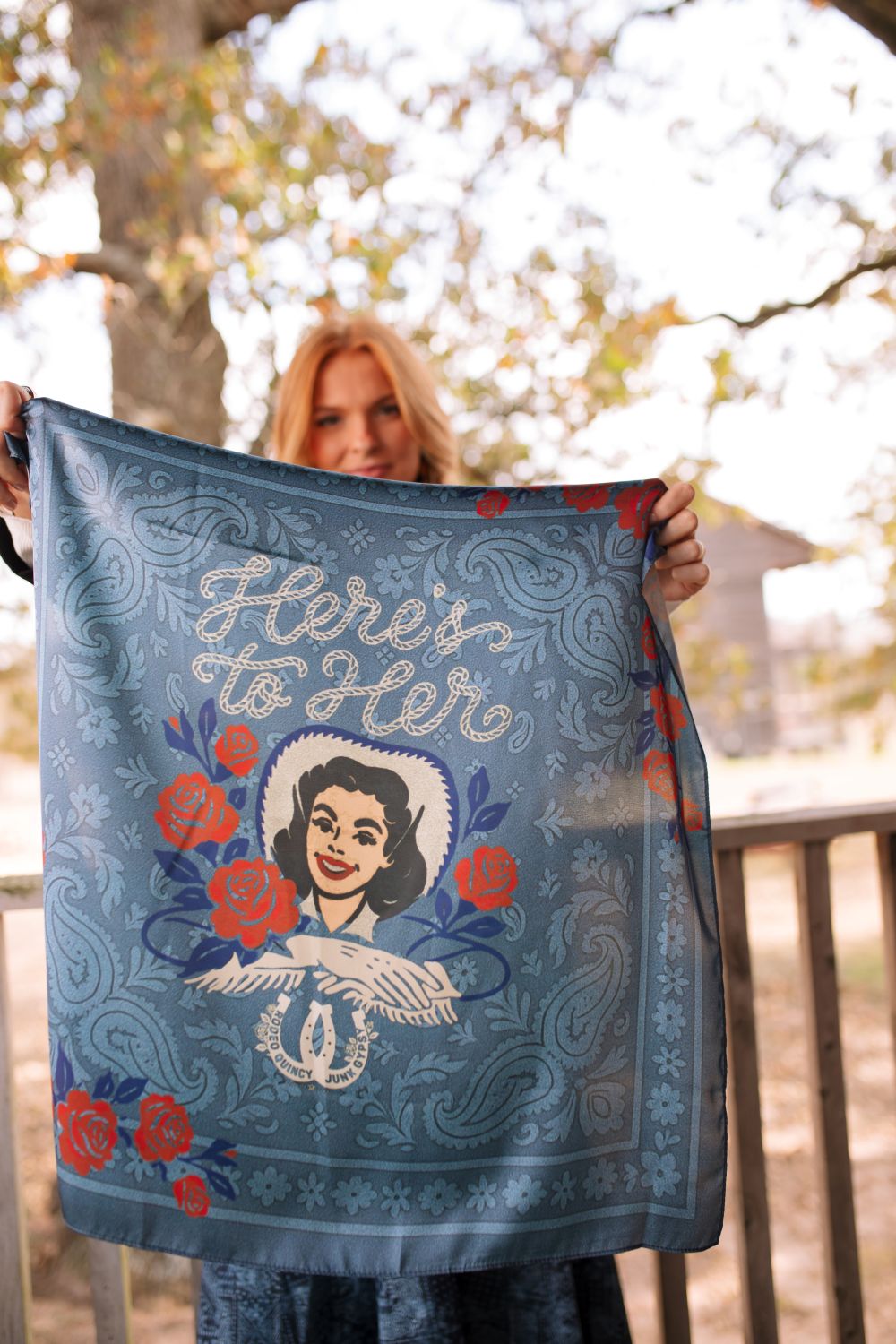 Person holding a decorative scarf with a design and text outdoors.