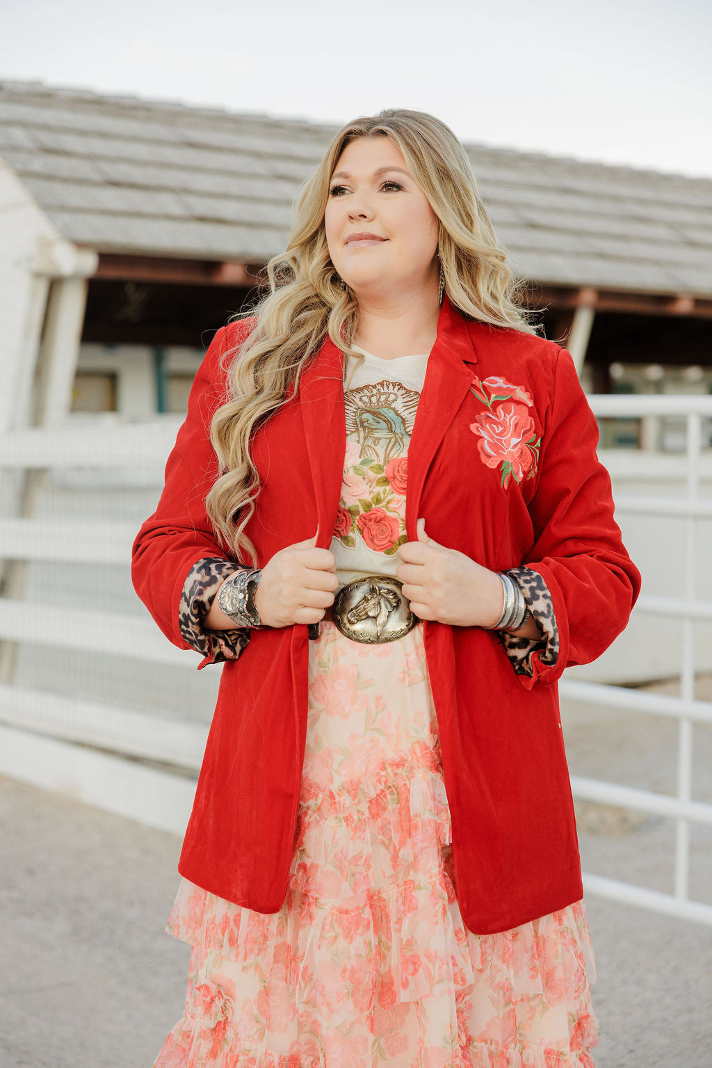 Woman wearing a red blazer over a floral dress with a belt, standing outdoors.