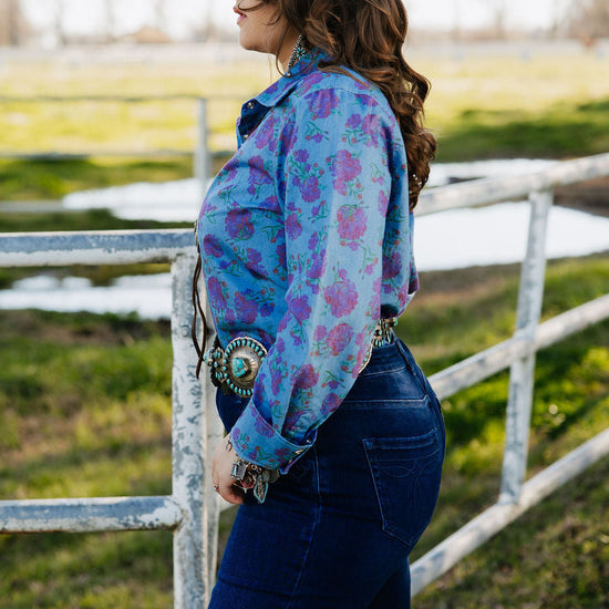 Woman wearing a colorful floral jacket with a large brooch standing in a field.
